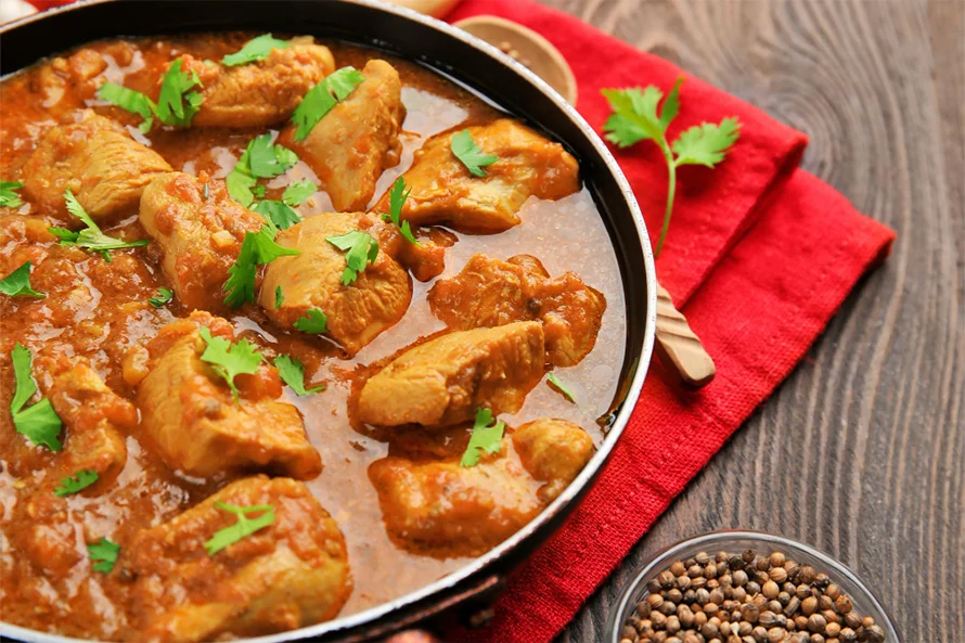 Creamy chicken korma curry garnished with herbs, served in a bowl.